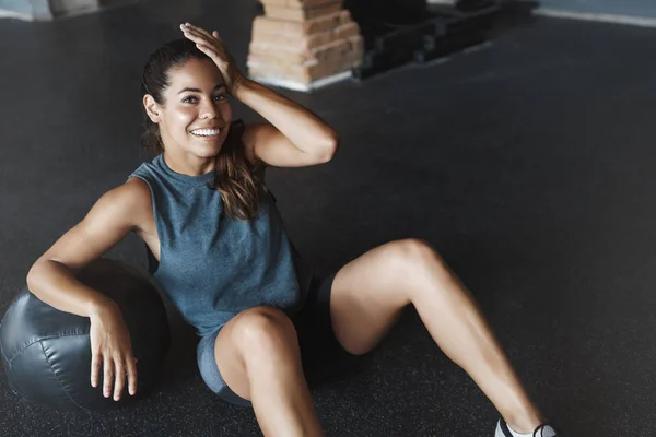 Recreación, bienestar y concepto deportivo. Motivada mujer atleta entrenamiento gimnasio club, sentarse cámara sonrisa gimnasio, limpiar el sudor de la frente, magra pelota medicina crossfit, sesión de entrenamiento de pilates intensos — Foto de Stock