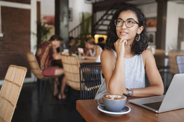 Vanlife, digital-nomad dan konsep freelance. Kreatif cukup perempuan bekerja pada remote, duduk di dalam kafe, minum cappucino, merenungkan konten artikel, duduk di dekat laptop, berpaling bijaksana, tersenyum — Stok Foto