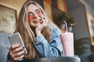 Sevimli caucasina kız arkadaşı portresi, akıllı telefon kullanarak yakındaki partilerde arama, erkek arkadaşı ile oturan ve lezzetli kokteyl zevk, geniş bir gülümseme ile bir kenara bakan, bir sonraki ne kadar düşünme