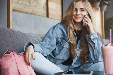 Taksi çağıran, arkadaşlarıyla oturan ve eve gitmek isteyen, ayakları çapraz kanepede oturan, akıllı telefonu kulağına yakın tutan, kamerada kaygısız gülümseyen, sıcak bir akşamkokteyl içen kız