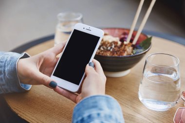 Asya restoranında dururken, udon yerken, Japon mutfağına aşık olurken, dışarıda tek başına yemek yerken akıllı telefon üzerinden indirim uygulamasını kullanan trendy urban kadın larının kırpılmış çekimi