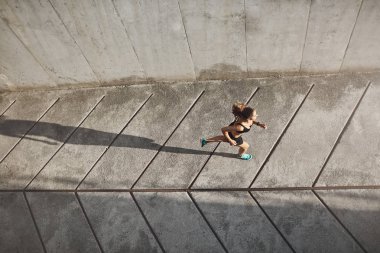 Havai görünümü siyah spor bra ve shrots beton yolda çalışan atletik kadın koşucu, günlük açık egzersiz sırasında sabah güneşine doğru hareket, fitness koşu maraton yarışmaya hazırlamak