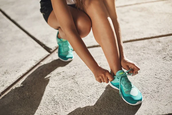 Yakın çekim kırpılmış kadın koşucu diz çökmüş beton yolda duran eğitmenler üzerinde ayakkabı bağcıkları bağlamak için, maraton için eğitim dışında duran jogger, sabah koşu bağcıkları sıkın emin olun — Stok fotoğraf