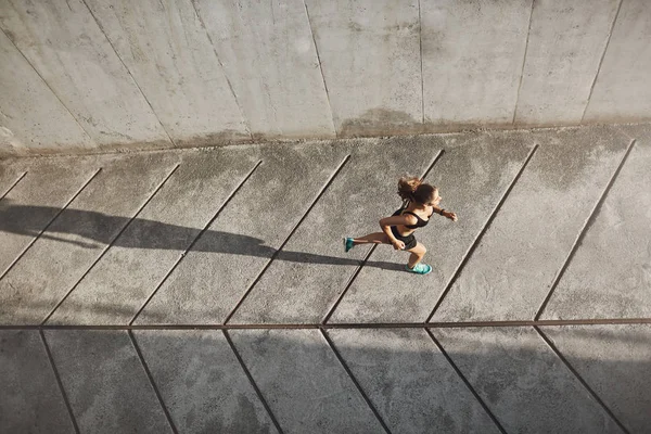 Overhead view athletic female jogger running on concrete track in black sportsbra and shrots, move towards morning sun during daily outdoor workout, fitness jogging prepare to marathon competition — Stock Photo, Image