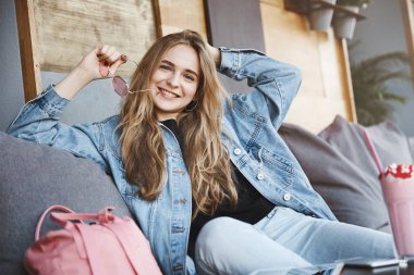 Eğlenceli bir şeyler yapalım. Kot ceketli güzel, kafede kanepede ürperen, elinde güneş gözlüğü ile oynayan, kız arkadaşıyla konuşurken geniş gülümseyen büyüleyici parti kız portresi