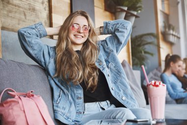 Kız kendini gurur hissediyor, son sınavı geçen ve lisans derecesi alıyorum. Moda güneş gözlüğü ve kot ceket güzel ve şık kentsel kadın, emin poz başının arkasında elleri ile oturan