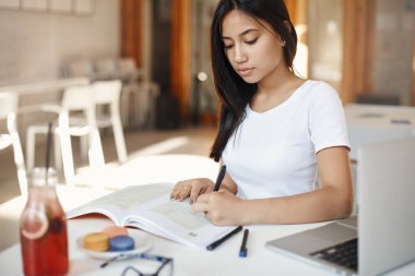 Pensive ve konsantre güzel genç kız öğrenci, notlar aşağı alarak, ödev yapma, internet eğitim sitesi üzerinden dil öğrenmek, kafede tek başına eğitim olarak dizüstü bilgisayar kullanarak. e-öğrenme kavramı