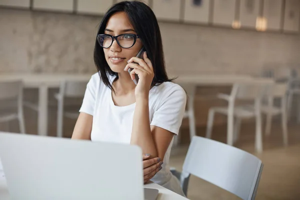 Side-shot drukke zelfverzekerde jonge gemachtigde vrouw in bril zitten alleen café tafel, bellen met smartphone, vond interessante Web-pagina met behulp van laptop controleren met site manager om details te weten — Stockfoto