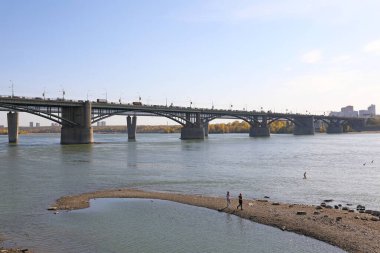 Novosibirsk, RUSSIA-20 Eylül 2020: Oktyabrsky köprüsünün arka planına karşı Ob Nehri 'nin kıyısında yürüyen kızlar