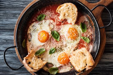 close-up view of gourmet fried eggs with cheese, bread and sauce in pan on wooden cutting board   clipart