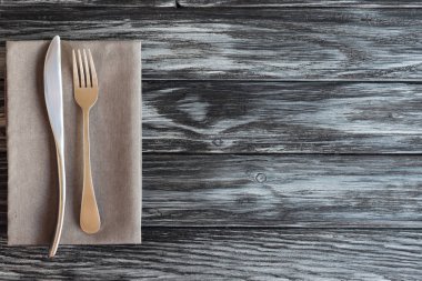 top view of fork and knife on napkin on wooden table clipart