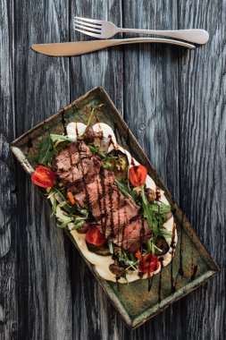 Üstten Görünüm lezzetli dilimlenmiş New York steak, sebze ve çatal bıçak üzerinde ahşap masa ile kavrulmuş 