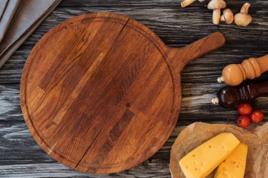 top view of empty wooden cutting board, spices, cheese and vegetables on table clipart