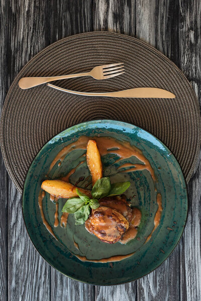 top view of gourmet ribeye beef steak with basil, fork and knife on wooden table
