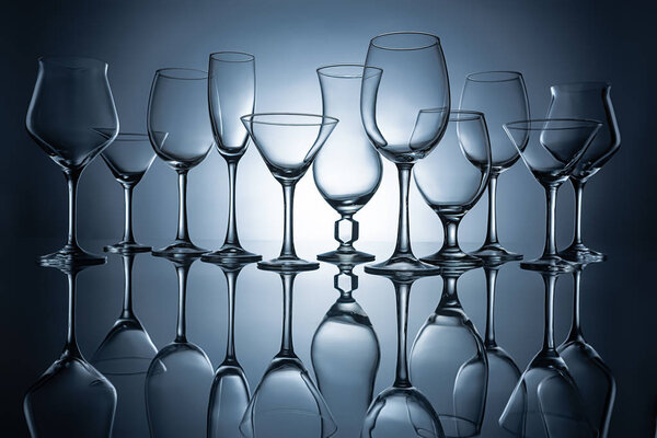silhouettes of different empty glasses with reflections, on grey