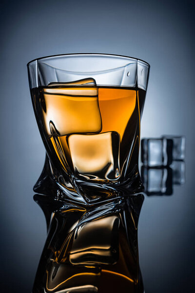 glass of whiskey with ice cubes with reflection, on dark grey background