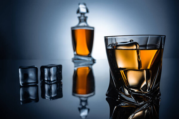 selective focus of glass with cognac, ice cubes and bottle, on grey