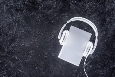 top view of white book and headphones on grey tabletop clipart