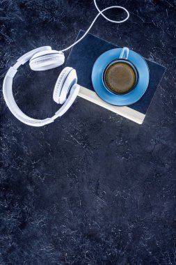 top view of book, white headphones and blue cup with coffee on grey tabletop clipart