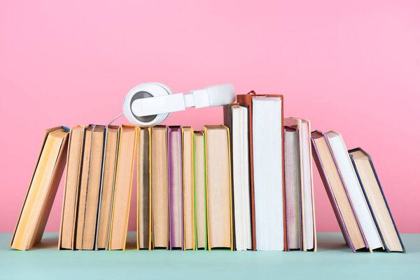 headphones on row of books on table on pink