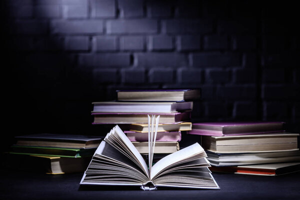 open book in front of stack of books on dark surface