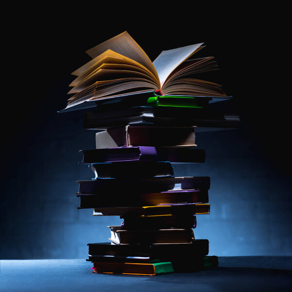 stack of colored books with open book on top on dark surface