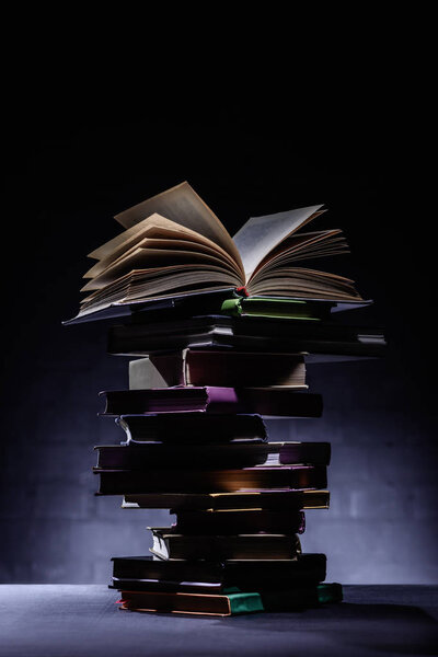 stack of books with open book on top on dark surface