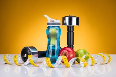 close-up view of dumbbells, measuring tape, bottle of water and apples on yellow clipart