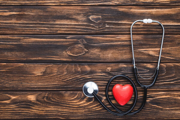 top view of stethoscope and red heart symbol on wooden table top  