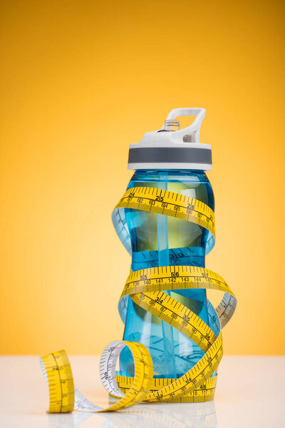 крупным планом вид спортивной бутылки с водой и измерительной лентой на желтый цвет
