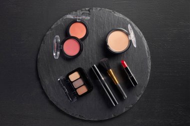 Makeup set with eye shadows and blush on round slate background clipart