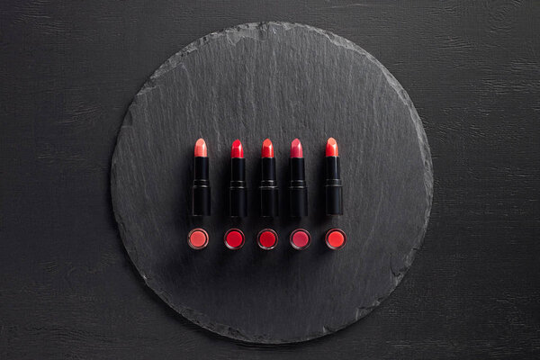 Row of red lipsticks on round slate background