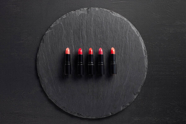 Row of lipsticks in pink and red tones on round slate background