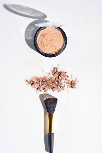Scattered face powder with brush on white background