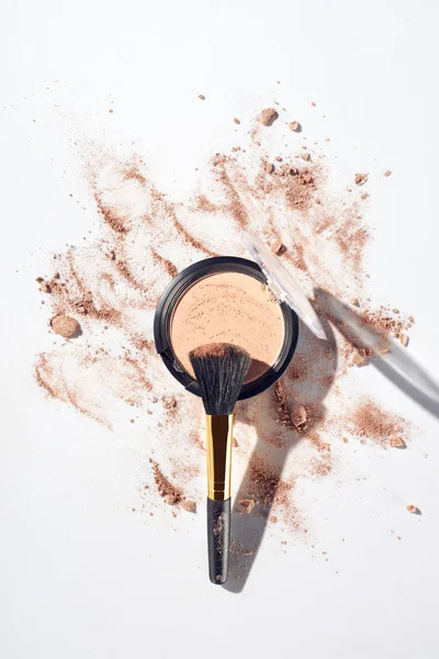 Broken and pressed face powder with brush on white background