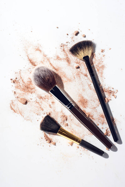 Broken face powder pieces and makeup brushes on white background