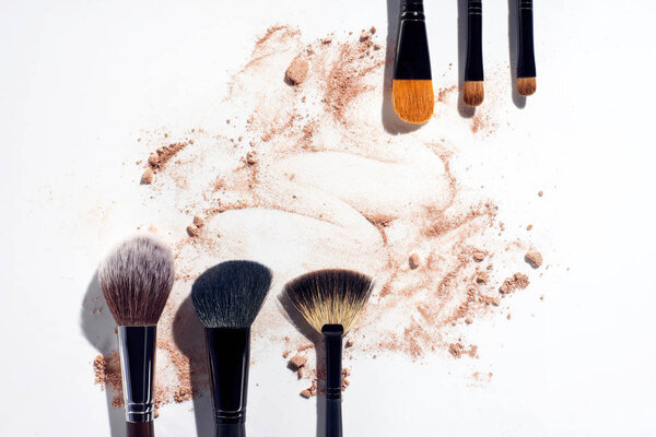 Frame of makeup brushes with powder foundation on white background