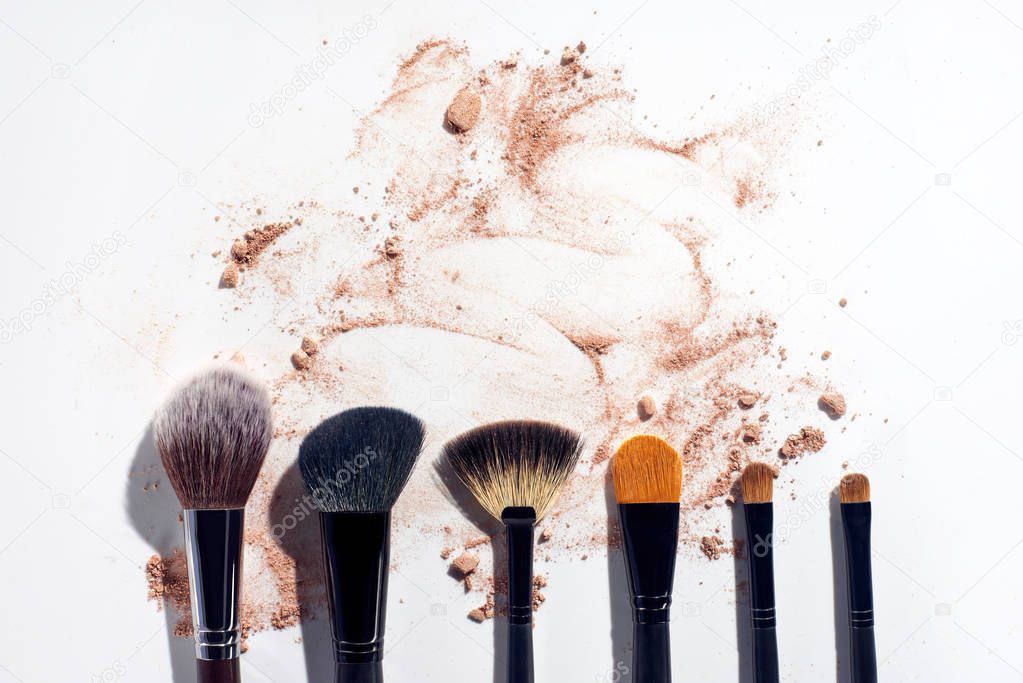 Set of brushes in a row on white background with scattered face powder