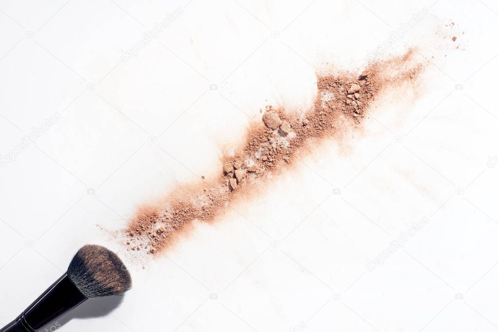 Line of scattered face powder and brush on white background