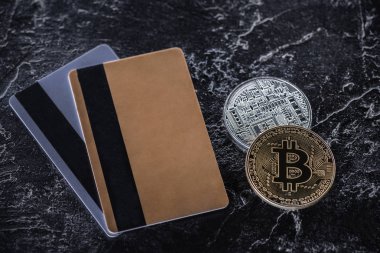 karanlık mermer yüzeyindeki kredi kartları ve bitcoins üstten görünüm
