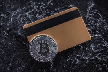 karanlık mermer masa üzerinde kredi kartı ve gümüş bitcoin üstten görünüm
