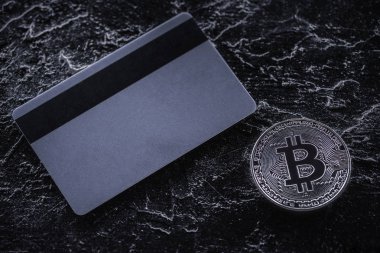 karanlık mermer masa üzerinde kredi kartı ve gümüş bitcoin üstten görünüm