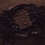Top view of chocolate with nuts in black crumpled paper on wooden table