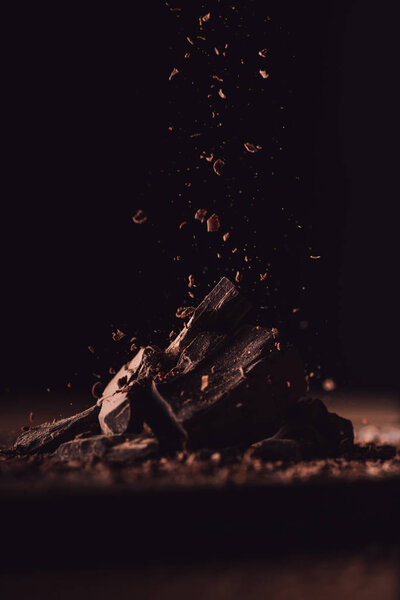 close up shot of grated dark chocolate falling on pieces of chocolate on black background 