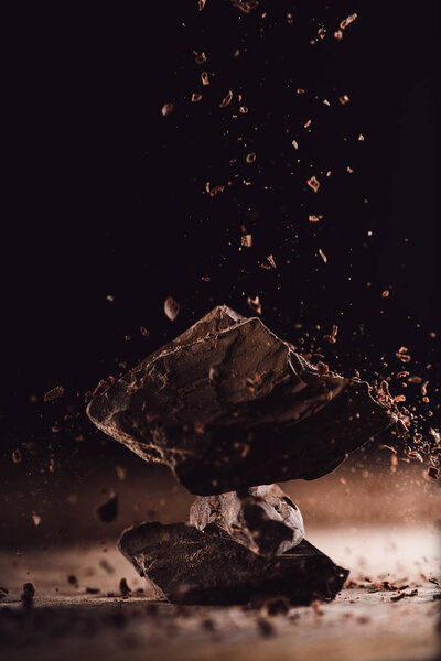  close up image of grated chocolate falling on pieces of chocolate on black background 