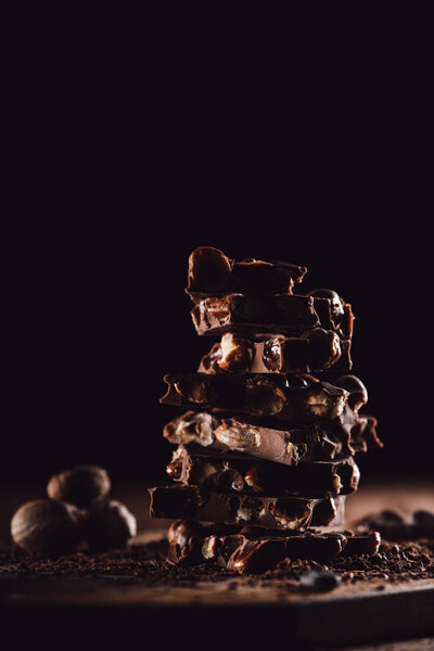 closeup shot of stack of chocolate pieces and nutmegs on black background 