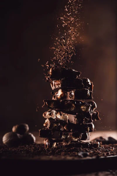 close up shot of nutmegs and grated chocolate falling on stack of chocolate pieces on wooden table