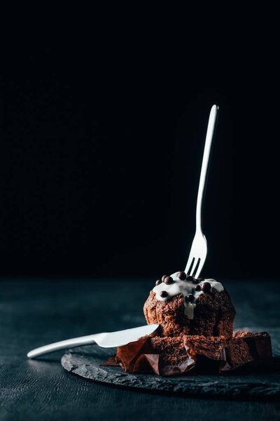 Delicious muffin with glaze and silverware set on dark background