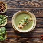 Draufsicht auf arrangierte vegetarische Sahnesuppe, Rosenkohl, Mandeln und frischen Brokkoli in Schalen auf Holzoberfläche