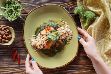 rendelenmiş badem ve ahşap masa üzerinde Brüksel lahanası ile kısmi vejetaryen salata tabak tutan kadın görünümünü servis